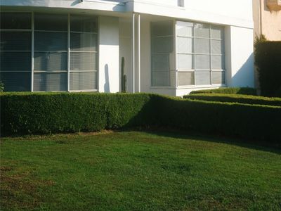 Lawn with trimmed hedges and a white house behind it